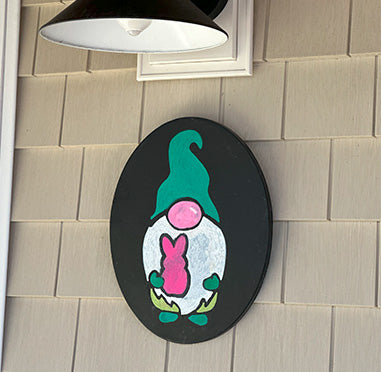 DIY outdoor gnome sign on an oval frameless chalkboard, featuring a colorful gnome painted with chalkboard stencil kits, displayed on a home's exterior wall