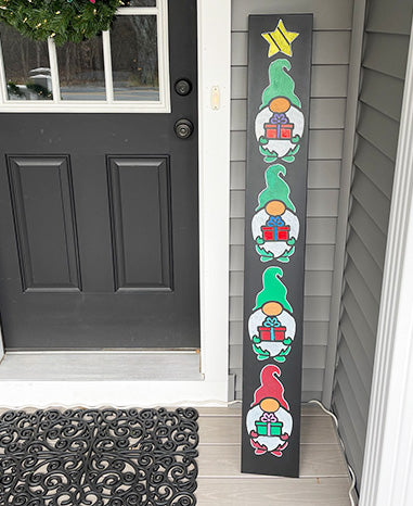 Handcrafted Christmas door sign featuring a vertical series of colorful gnomes with  presents, created using a Plata Chalkboards outdoor chalkboards and magnetic gnome stencils and erasable paint pens to create a DIY Christmas sign