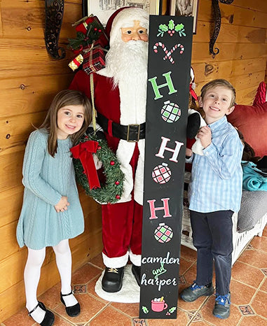 User-generated Christmas welcome sign with 'HO HO HO' crafted on a large outdoor chalkboard using Plata Chalkboard's magnetic letter stencils, Christmas stencils, and painting pens, featuring two children and a Santa Claus figure