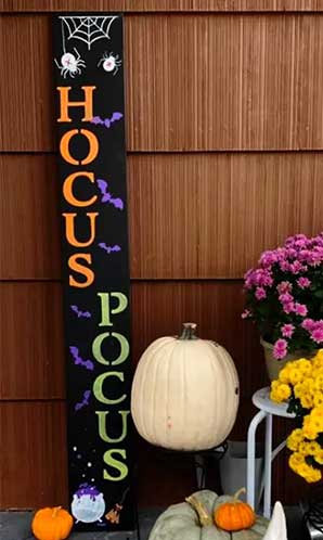 Handmade outdoor Halloween sign displaying 'HOCUS POCUS' in bold white letters against a black background, decorated with spider and bat designs, made using magnetic chalkboard stencils and erasable markers  to craft a DIY Halloween sign