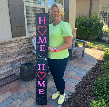 User-generated 'Home Sweet Home' DIY welcome sign with heart designs, crafted on a Plata Outdoor Chalkboard using magnetic letter stencils and paint pens, held by a smiling woman