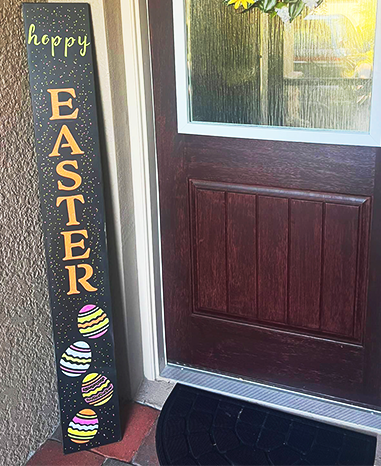 Outdoor blackboard sign reading 'HAPPY EASTER' in colorful letters, decorated with vibrantly painted Easter eggs, crafted with Easter stencils, placed beside a front door
