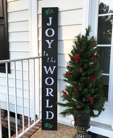 DIY Christmas sign reading 'JOY TO THE WORLD' in white letters on a Plata Porch chalkboard, crafted with paint pens, magnetic letter stencils and Christmas stencils, next to a decorated tree