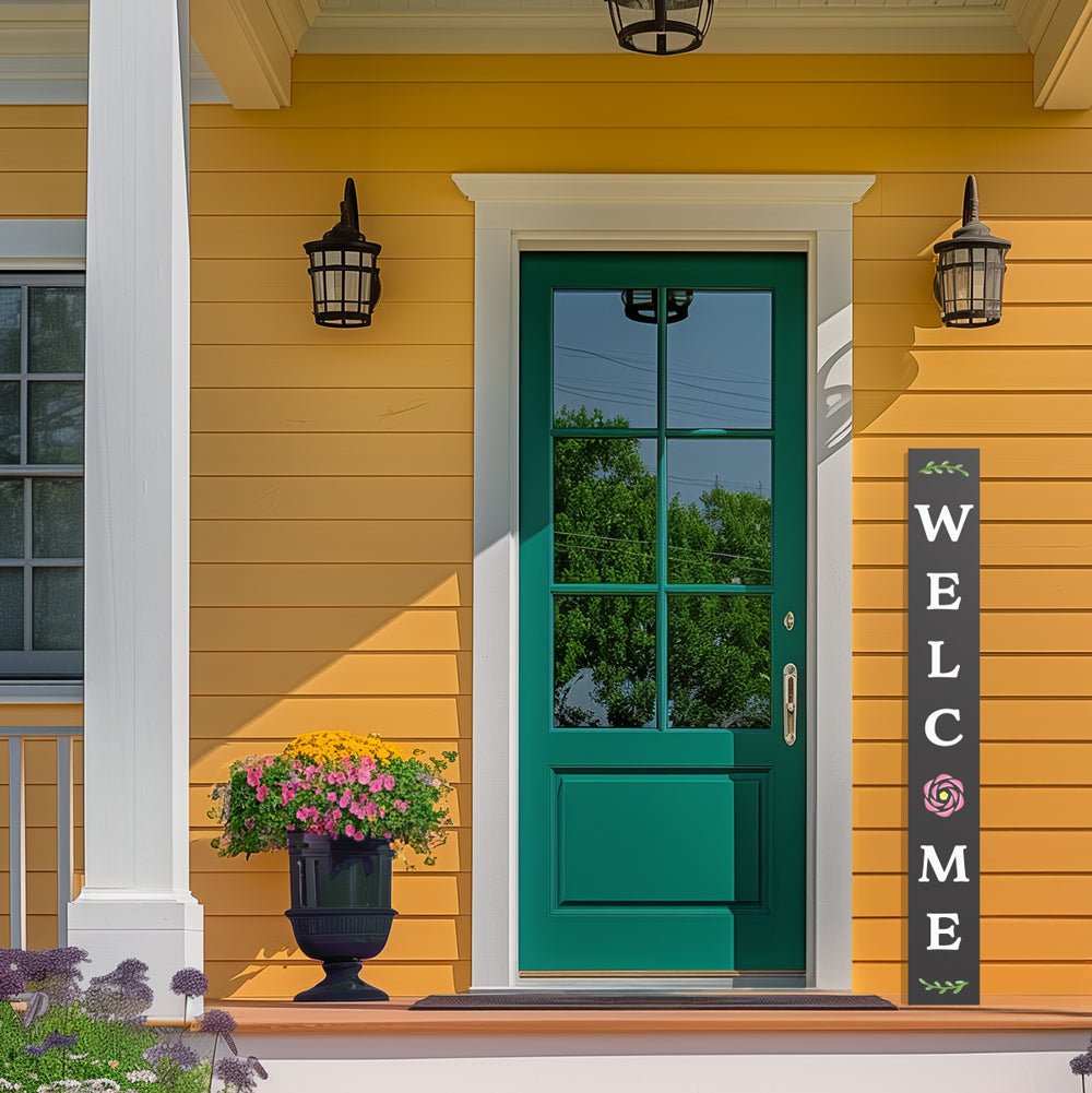 A large chalkboard welcome sign leans next to the green front door  of a yellow farmhouse, the DIY welcome sign is crafted with letter stencils on a chalkboard
