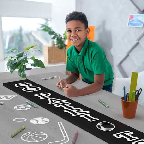 Boy enjoying a sports craft project making a football sign on a large chalkboard with magnetic letter stencils and sports stencils to create a &#39;Go Patriots&#39; football sign