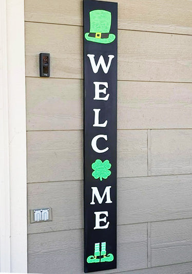 Handmade vertical welcome sign, using magnetic chalkboard stencils, displays 'WELCOME' in bold white letters with a vibrant green leprechaun hat and shamrock, adding a festive Irish welcome to entryway