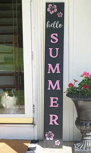 Outdoor chalkboard porch sign displaying 'hello SUMMER' stenciled bold, pink letters, accented with pink tropical flowers standing by a white door with a cat peeking through, created with chalkboard letter stencils and flower stencils to create a tropical summer welcome sign