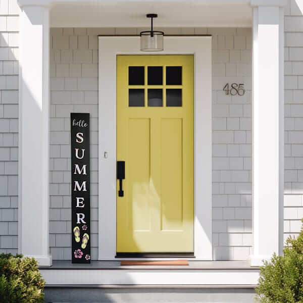 Hello Summer vertical porch welcome sign chalkboard decorated with flip flops and tropical flowers leaning next to a yellow front door of a modern farmhouse