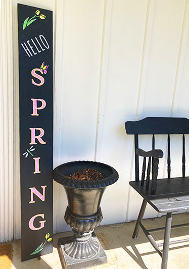 Large outdoor chalkboard sign crafted to say 'Hello Spring' in pink letters using large letter stencils with decorated with yellow tulips and butterflies using spring stencils and chalk paint markers
