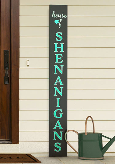 Large outdoor blackboard sign placed by a front door reads 'house of SHENANIGANS' in tall white letters with a shamrock detail, creating a playful Irish greeting sign for St. Patrick's Day