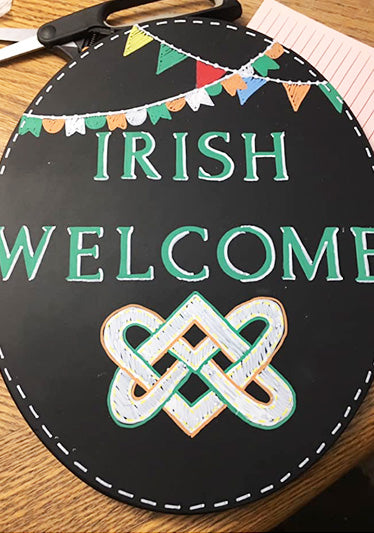 Oval chalkboard sign with 'IRISH WELCOME' in green letters and a colorful Celtic knot, created with magnetic letter stencils and chalk markers for an easy St. Patrick's Day craft..