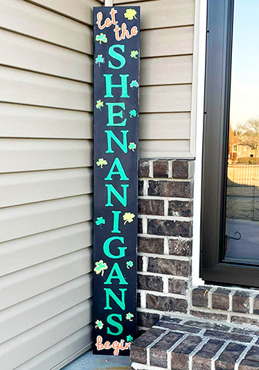 Outdoor blackboard sign with 'Let the SHENANIGANS Begin' stenciled in green letters, interspersed with shamrocks, for a funny St. Patrick's Day DIY sign