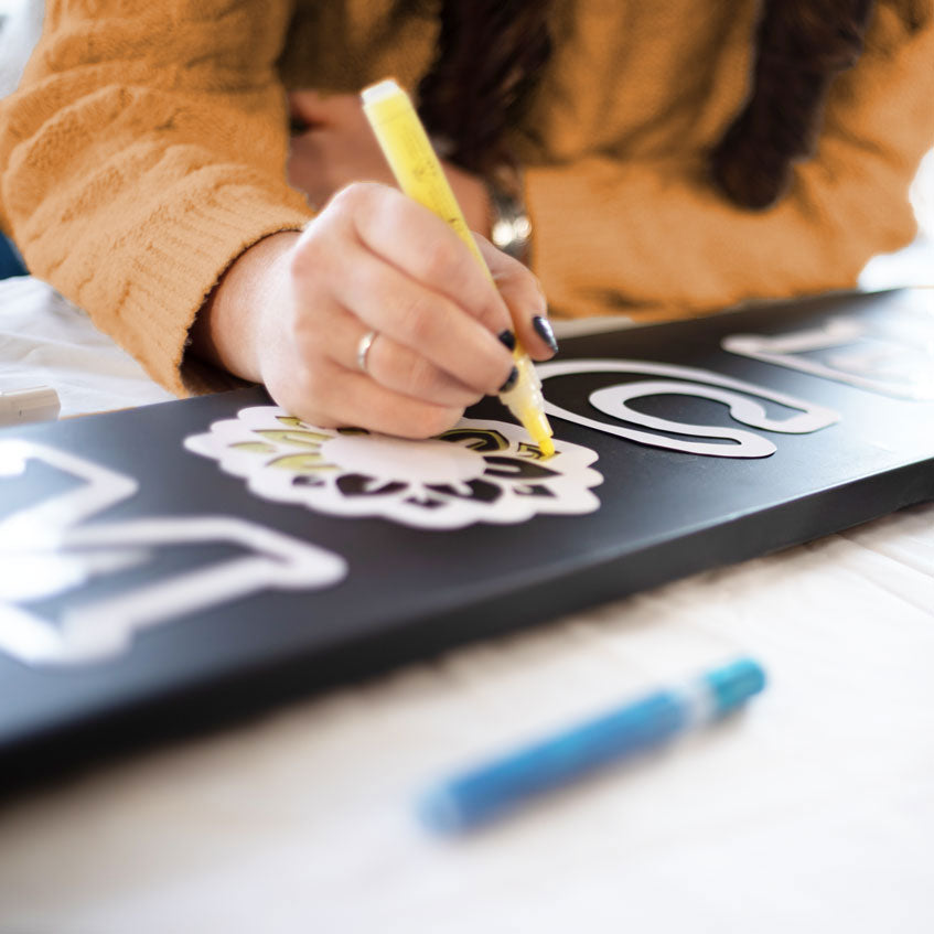 woman crafting a DIY welcome sign porch chalkboard with large letter stencils and sunflower stencil using Plata Chalkboards craft kit