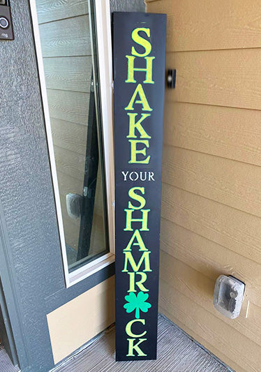DIY St. Patrick's Day chalkboard porch sign stenciled 'SHAKE YOUR SHAMROCK' with bold white letters and vibrant green shamrocks, exemplifying easy and custom St. Patrick's Day Door Sign