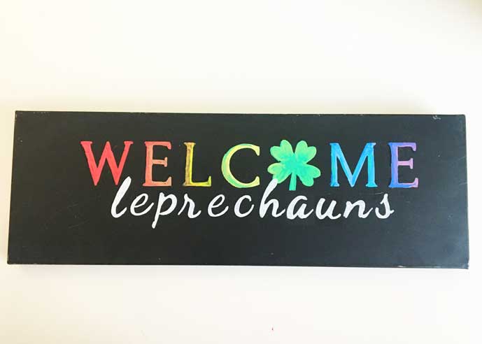 hanging chalkboard sign with 'WELCOME leprechauns' in colorful rainbow letters, accented with a green shamrock, crafted with magnetic stencils and chalk markers for a St. Patrick's Day door sign