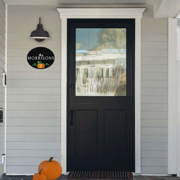 A Plata Oval Holiday Chalkboard Stencil Craft Kit for Adults Stenciled with a last name and a pumpkin hanging horizontally under a farmhouse light next to front door
