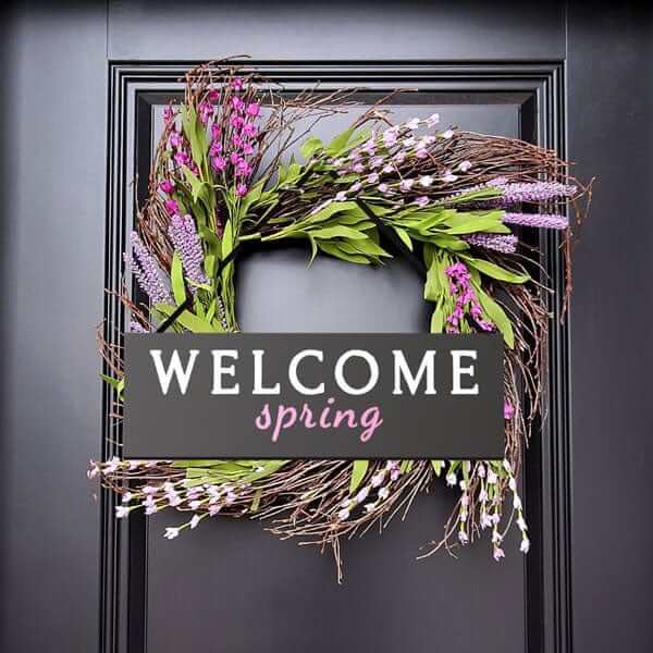 Welcome sign chalkboard hung on a wreath on a black front door stenciled &#39;welcome spring&#39; using letter stencils and chalk paint pens