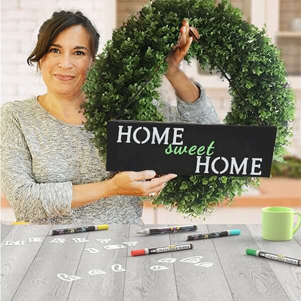 Woman holding wreath with welcome sign chalkboard stenciled 'Home Sweet Home' with chalkboard letter stencils and erasable chalk markers